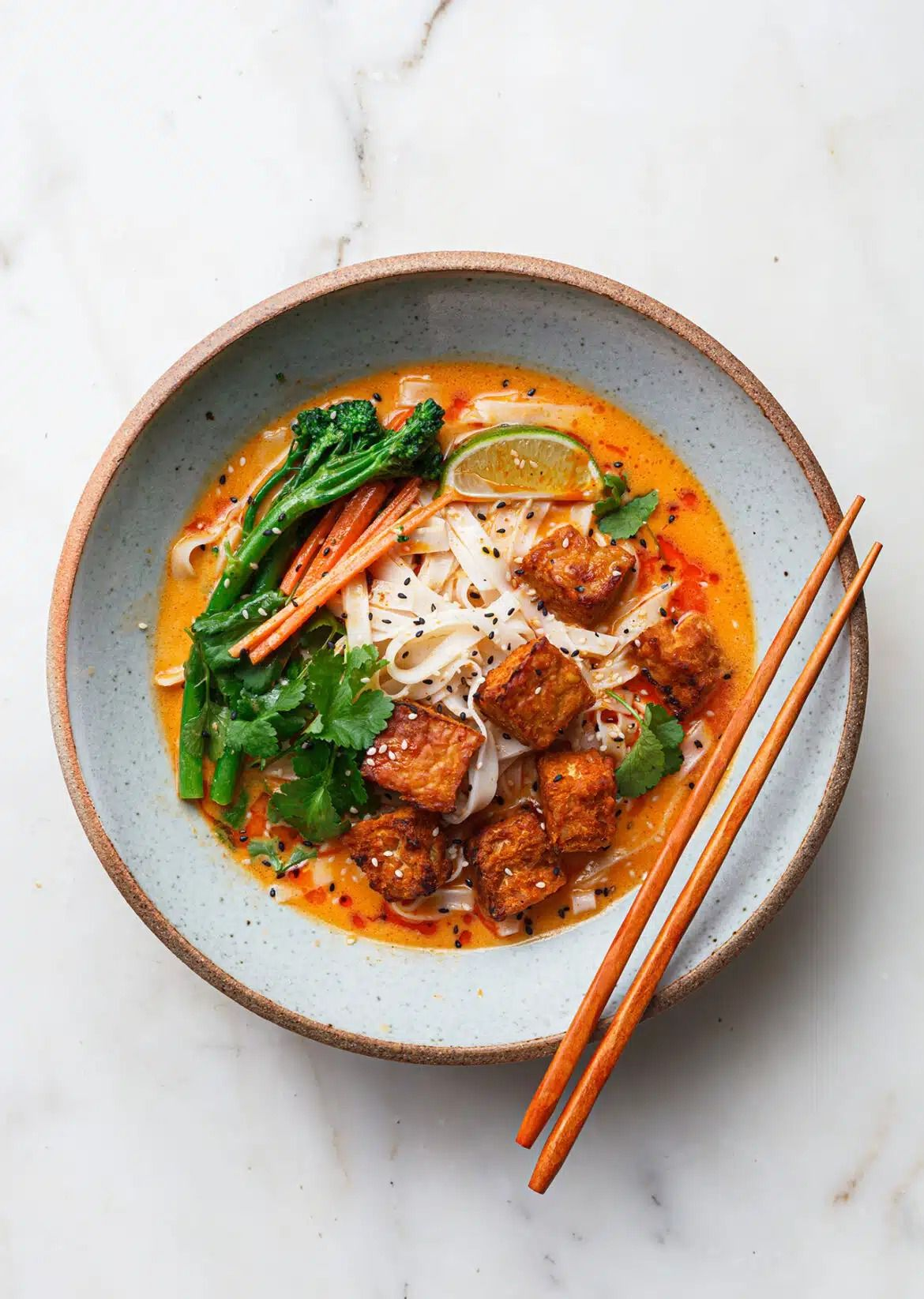 Vibrant ramen bowl with crispy tofu, fresh greens, lime, and chopsticks in rich orange broth